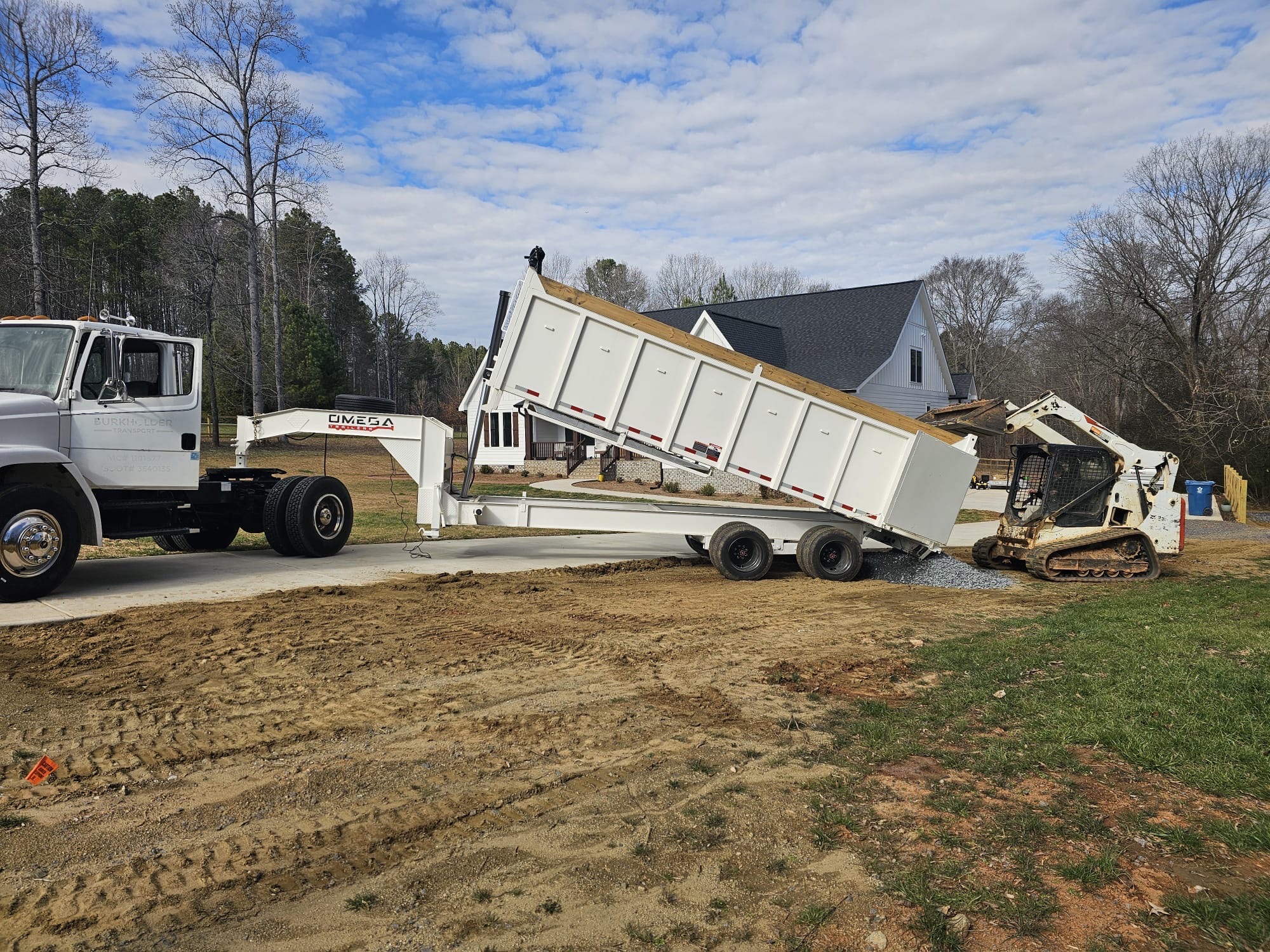Dump trailer delivering gravel for a new driveway while a track loader spreads it