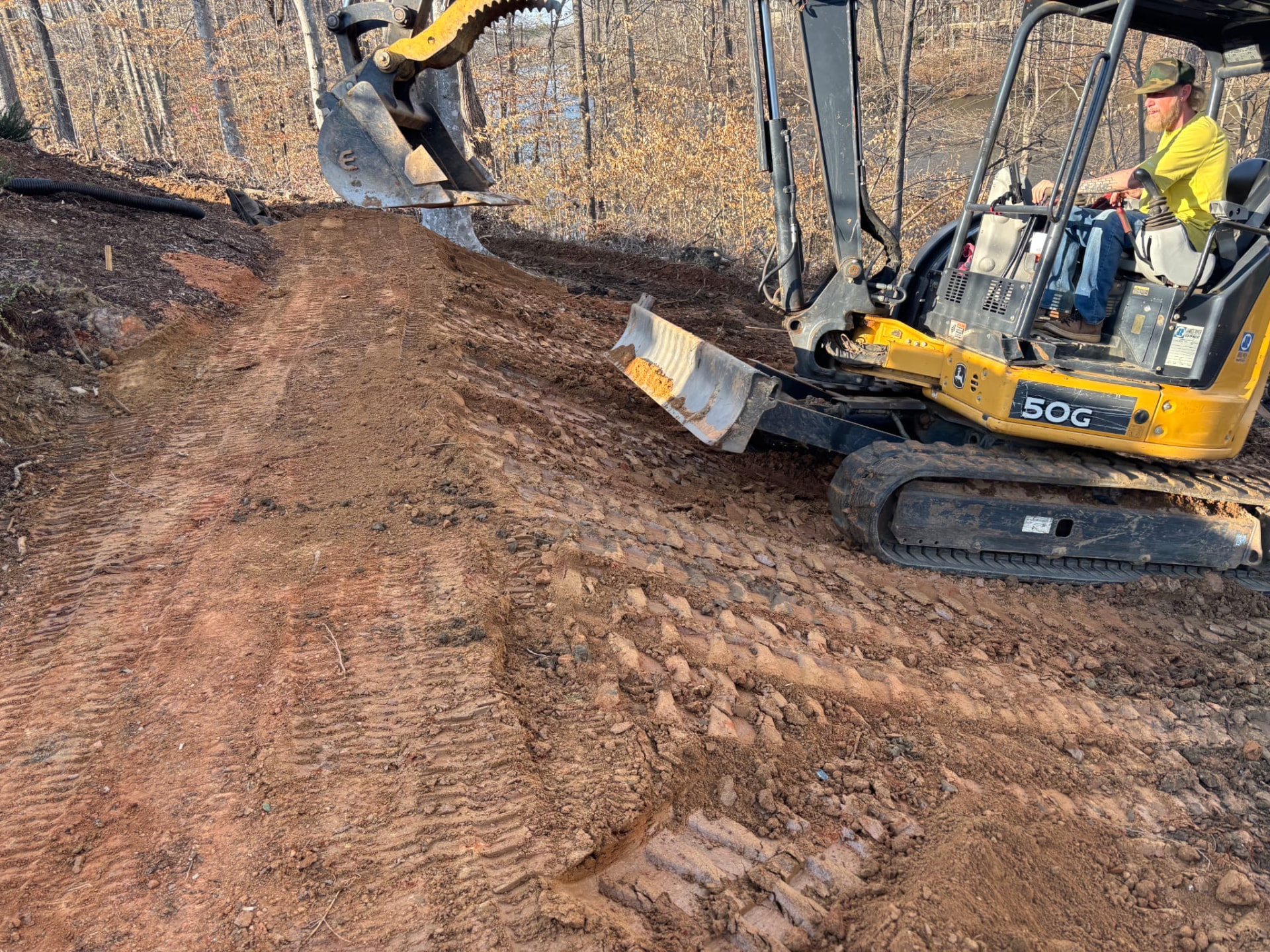 Mini excavator grading a slope on a wooded lot